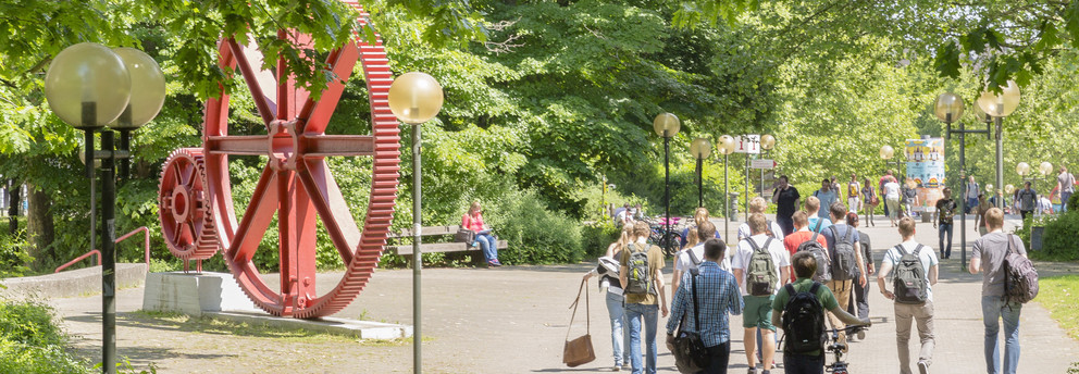 Students walking across Campus Nord. In The background there is a red sculpture of large gears.