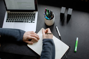 A student working at a table with a laptop, pencils and a notebook.